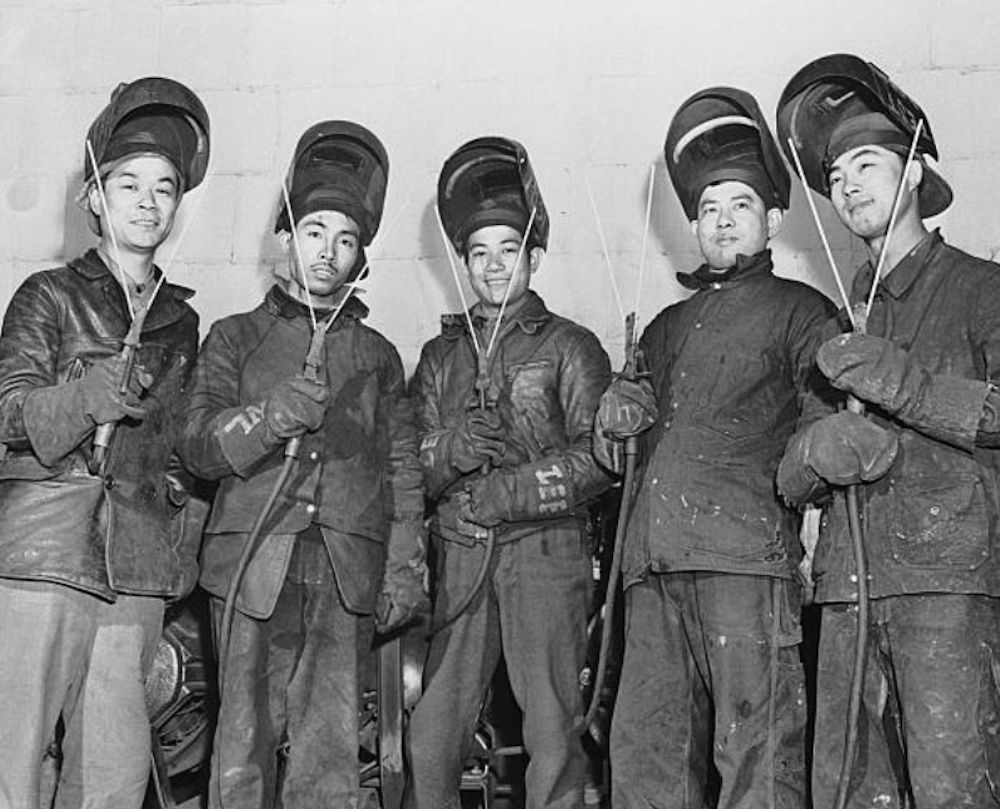 5/13/1943-Port Newark, NJ: Born in conquered Canton, but now good Americans all, these five Chinese are helping build destroyer escorts at the Federal Shipbuilding Yards in Port Newark. They make 'V' signs with welding rods, fitting two into each welder's electrode. Left to right are Jing Lee, former waiter of Brooklyn; Wesley Fong Lau, New York Food dealer; Gar Gee Lee, Astoria waiter; Wong Jung Shew, laundryman of Scarsdale, New York, and young Wah Yueb, ex-cook of Newark.
Photo from Bettmann
